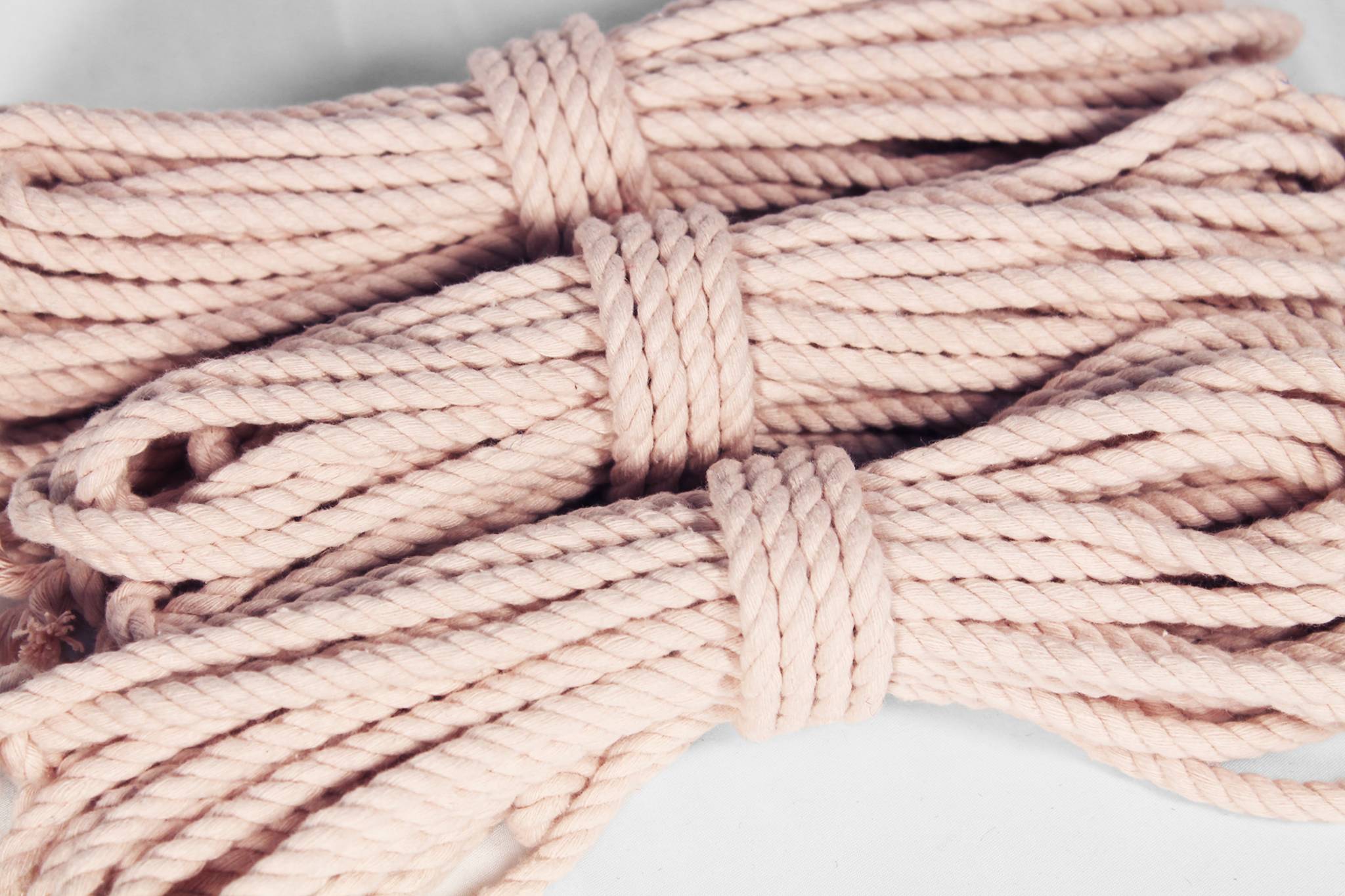 A close-up of several coiled strands of thick twisted rope in a pale blush pink color, arranged on a light neutral background.